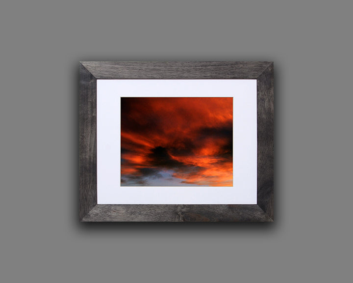 Nature photography print of a fiery sunset with orange and black clouds shown with a black frame called Burst by Loud Hue