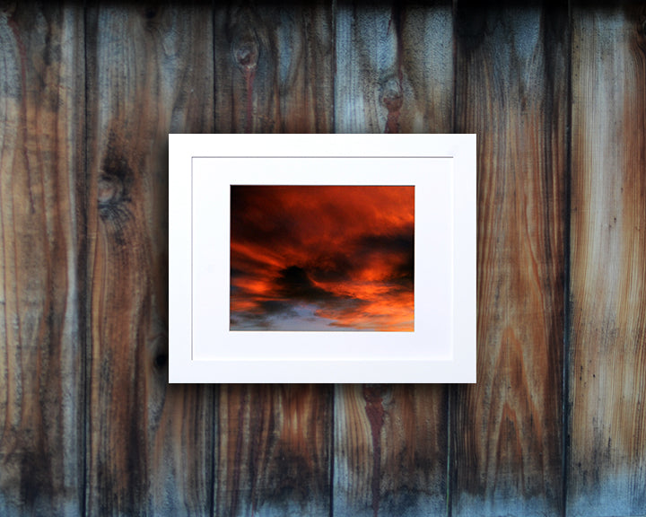 Nature photography print of a fiery sunset with orange and black clouds shown mounted with a white frame called Burst by Loud Hue