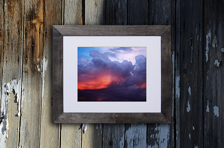 Nature photography print of a turbulent multicolor sunset shown with a black frame called Divine by Loud Hue