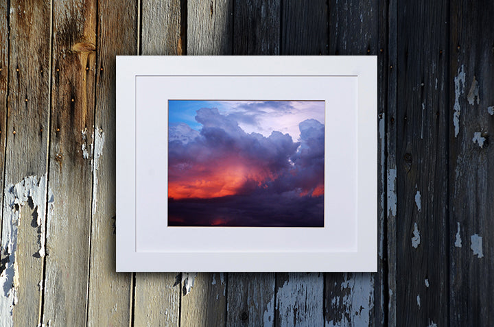 Nature photography print of a turbulent multicolor sunset shown with a white frame called Divine by Loud Hue
