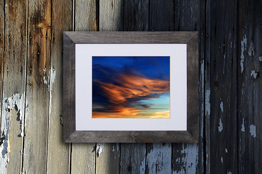 Nature photography print of a beautiful sunset with warm blue and gold hues shown with a black frame called Golden Wings by Loud Hue