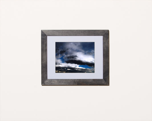 Nature photography print of a dramatic blue, gray and black cloudy sky shown in a black frame called Cotton by Loud Hue