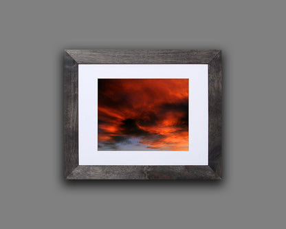 Nature photography print of a fiery sunset with orange and black clouds shown with a black frame called Burst by Loud Hue