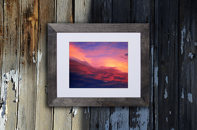 Nature photography print of a luminous blue, pink, yellow and red sunset shown with a black frame called Purple by Loud Hue