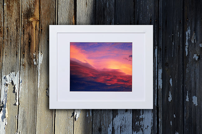 Nature photography print of a luminous blue, pink, yellow and red sunset shown with a white frame called Purple by Loud Hue